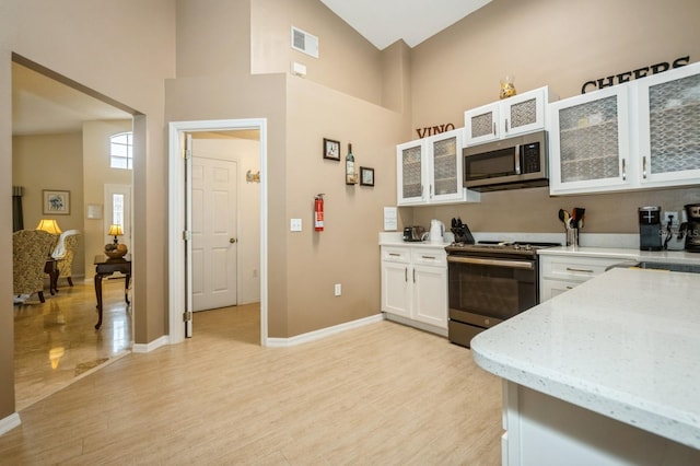 kitchen featuring white cabinetry, high vaulted ceiling, light hardwood / wood-style flooring, and stainless steel appliances