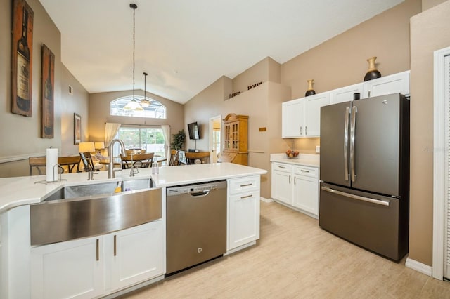 kitchen featuring white cabinets, appliances with stainless steel finishes, vaulted ceiling, decorative light fixtures, and light wood-type flooring