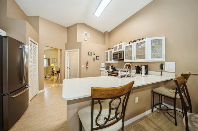 kitchen with vaulted ceiling, kitchen peninsula, a breakfast bar area, appliances with stainless steel finishes, and white cabinetry