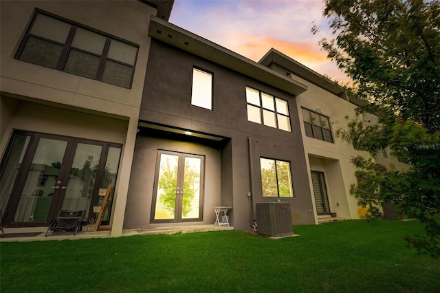 back house at dusk with central air condition unit, french doors, and a lawn