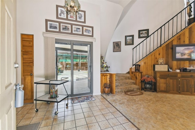 tiled foyer with wood walls, high vaulted ceiling, and an inviting chandelier