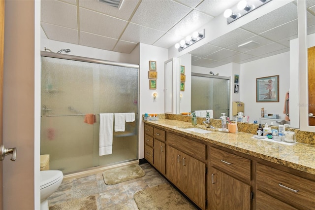 bathroom featuring a paneled ceiling, large vanity, toilet, a shower with shower door, and tile floors