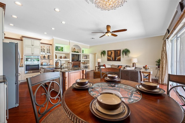 dining area with ornamental molding, built in features, ceiling fan with notable chandelier, and dark hardwood / wood-style flooring