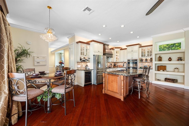 kitchen with appliances with stainless steel finishes, a kitchen island with sink, dark hardwood / wood-style floors, beverage cooler, and backsplash