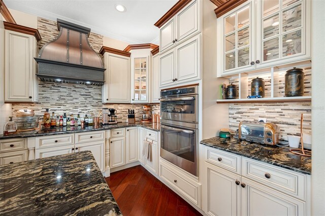 kitchen with dark stone counters, tasteful backsplash, double oven, and custom exhaust hood