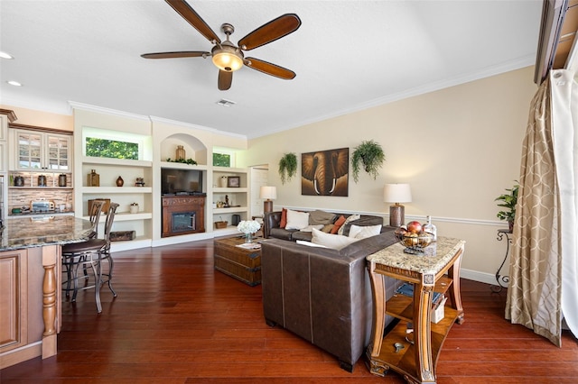 living room with built in features, ceiling fan, dark hardwood / wood-style flooring, and crown molding