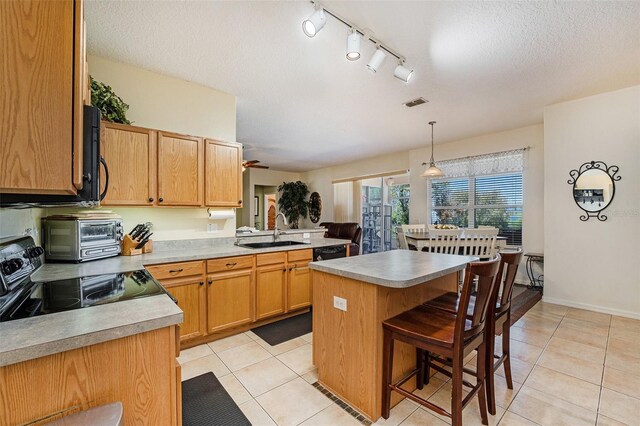 kitchen with a breakfast bar, stove, track lighting, pendant lighting, and sink