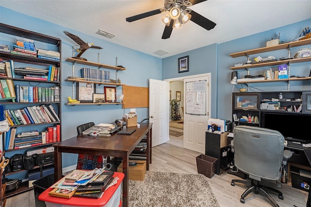 office area with light hardwood / wood-style floors, ceiling fan, and a textured ceiling