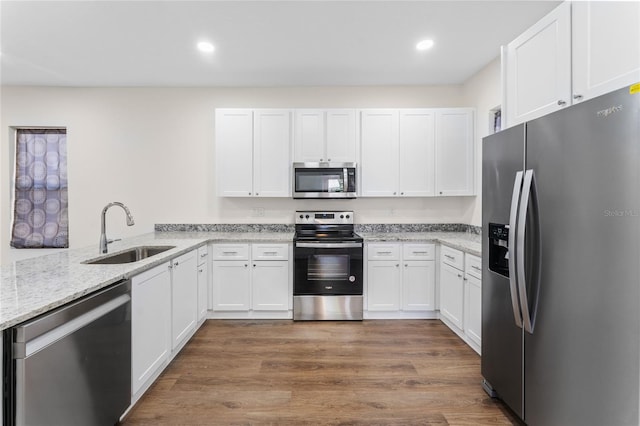 kitchen with light stone countertops, stainless steel appliances, white cabinets, sink, and light wood-type flooring