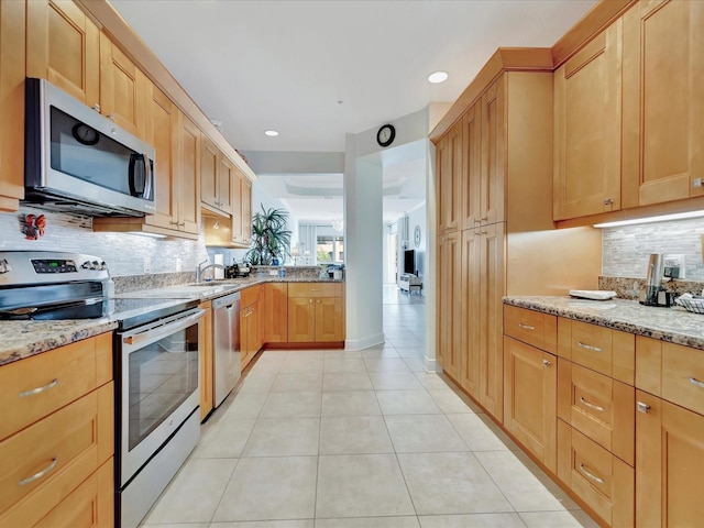 kitchen featuring light stone countertops, backsplash, sink, stainless steel appliances, and light tile floors