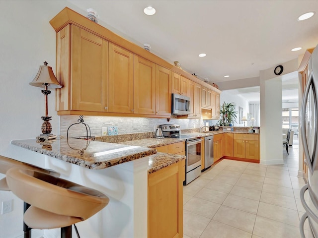 kitchen featuring kitchen peninsula, light stone countertops, backsplash, a breakfast bar, and stainless steel appliances