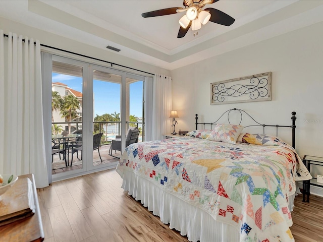 bedroom featuring access to outside, ceiling fan, a raised ceiling, and light wood-type flooring