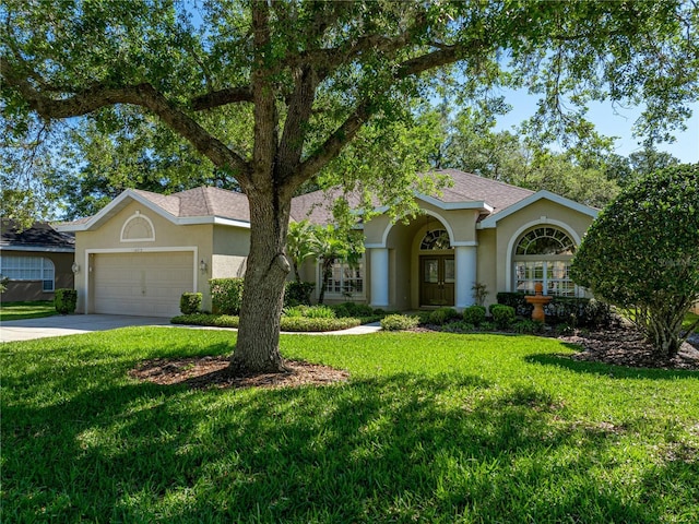 view of front facade with french doors, stucco siding, a front yard, a garage, and driveway