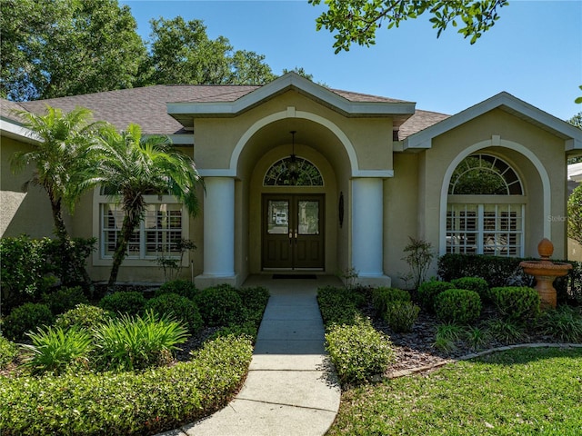 view of exterior entry with french doors, roof with shingles, and stucco siding