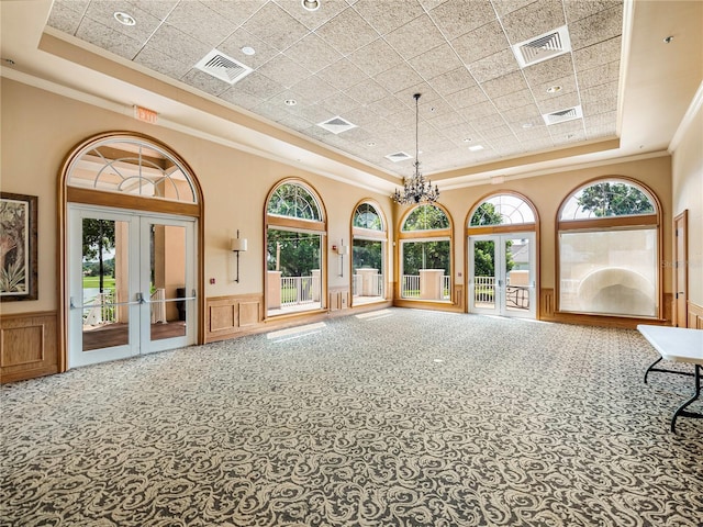 interior space with a wainscoted wall, french doors, a raised ceiling, and visible vents