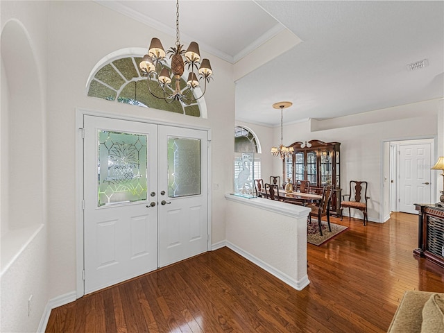 entrance foyer with dark wood-type flooring, ornamental molding, and a chandelier