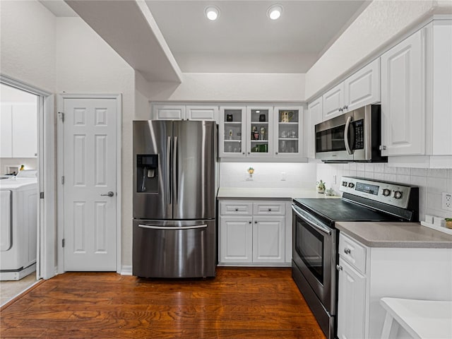 kitchen with appliances with stainless steel finishes, glass insert cabinets, washer / dryer, and white cabinets