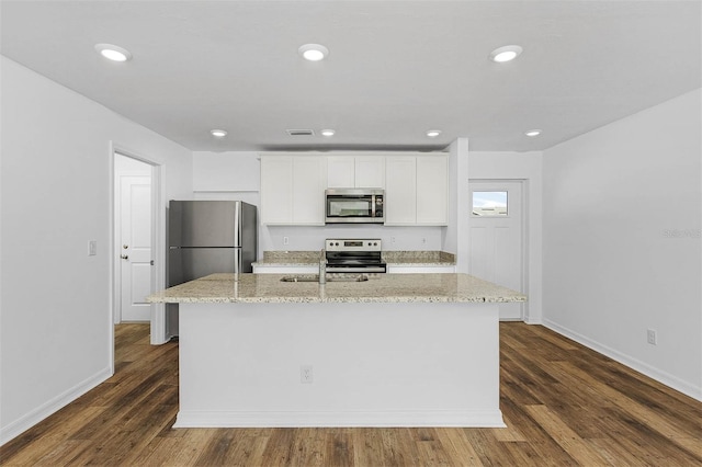 kitchen with appliances with stainless steel finishes, light stone counters, a kitchen island with sink, dark hardwood / wood-style floors, and white cabinets