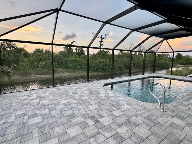 pool at dusk featuring a water view, glass enclosure, and a patio area