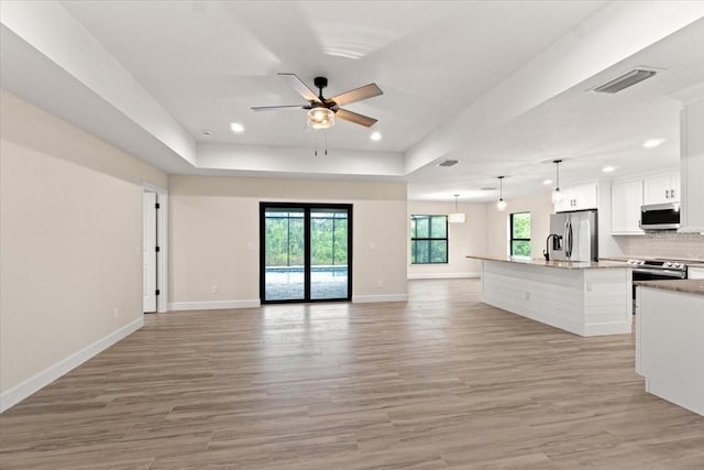 unfurnished living room with ceiling fan, a tray ceiling, and light wood-type flooring