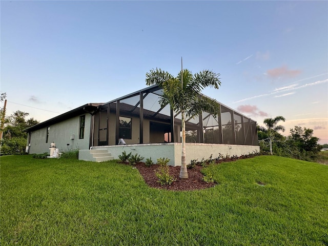 property exterior at dusk featuring a yard and glass enclosure