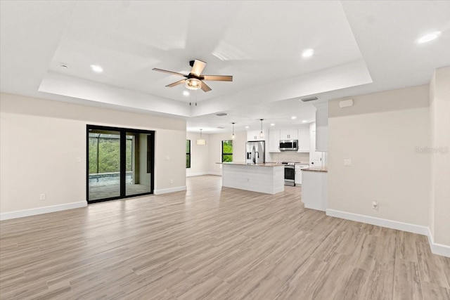 unfurnished living room with ceiling fan, a raised ceiling, and light hardwood / wood-style flooring