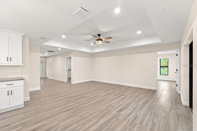 unfurnished living room with a raised ceiling, ceiling fan, and light wood-type flooring