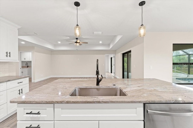 kitchen featuring white cabinetry, a tray ceiling, stainless steel dishwasher, light stone counters, and sink