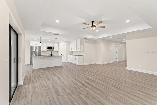 unfurnished living room featuring a raised ceiling, ceiling fan, sink, and light hardwood / wood-style flooring