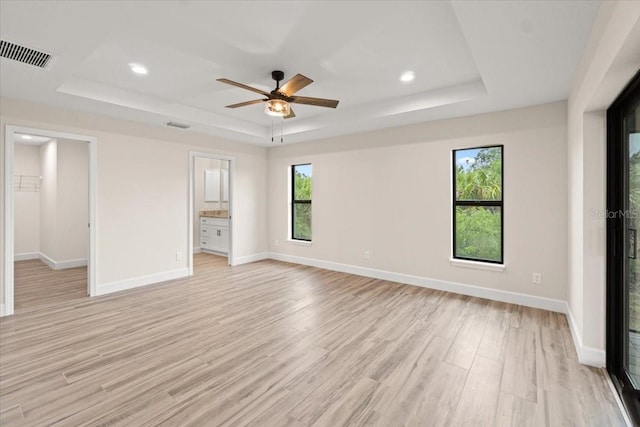 unfurnished bedroom with ceiling fan, ensuite bathroom, light hardwood / wood-style floors, and a raised ceiling