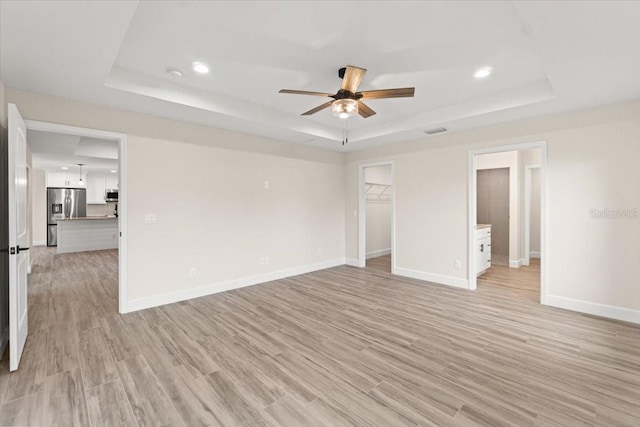 unfurnished room featuring a raised ceiling, light wood-type flooring, and ceiling fan