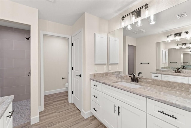 bathroom featuring toilet, vanity, a tile shower, and hardwood / wood-style floors