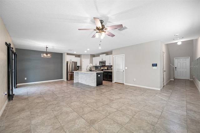 kitchen with a barn door, a center island with sink, visible vents, a ceiling fan, and appliances with stainless steel finishes