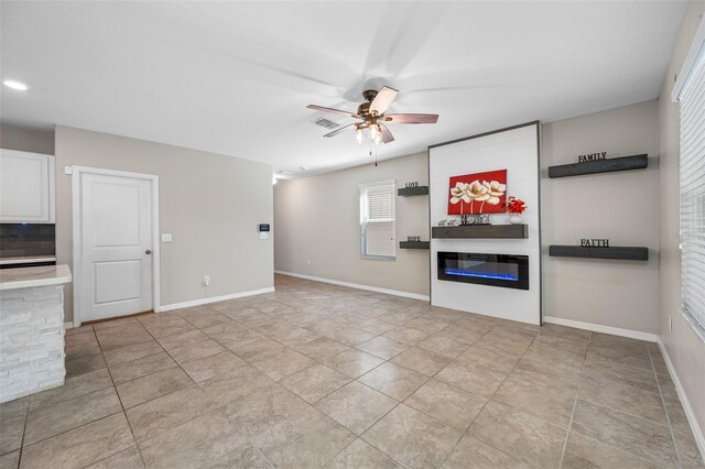 unfurnished living room featuring light tile patterned floors, visible vents, a ceiling fan, baseboards, and a glass covered fireplace