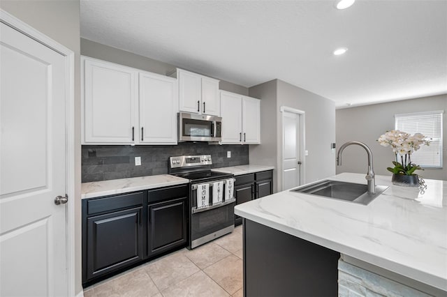 kitchen featuring light stone countertops, stainless steel appliances, a sink, white cabinets, and decorative backsplash