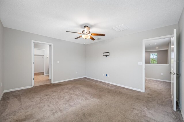 carpeted spare room with a textured ceiling, visible vents, a ceiling fan, and baseboards