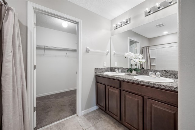 bathroom featuring a textured ceiling, a spacious closet, visible vents, and a sink