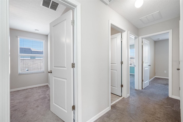 corridor with carpet, visible vents, and a textured ceiling