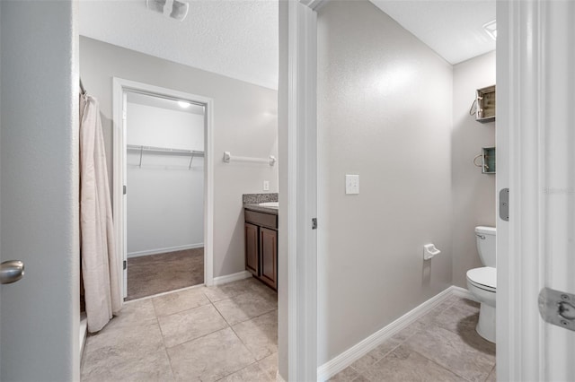 full bathroom with a walk in closet, toilet, vanity, a textured ceiling, and baseboards