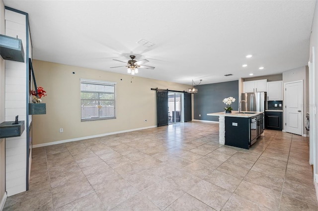 kitchen with a barn door, a ceiling fan, open floor plan, light countertops, and an island with sink