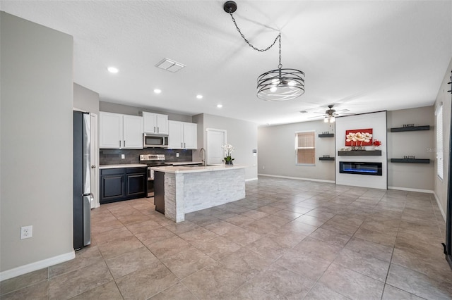 kitchen featuring light countertops, backsplash, appliances with stainless steel finishes, a glass covered fireplace, and white cabinets