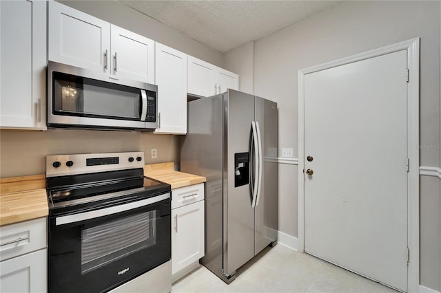 kitchen with stainless steel appliances, white cabinetry, wood counters, and a textured ceiling