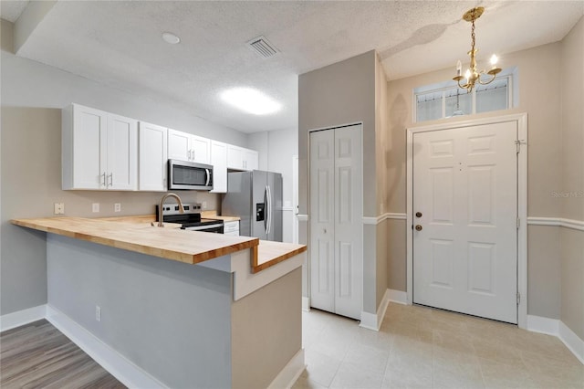 kitchen with white cabinets, butcher block counters, stainless steel appliances, hanging light fixtures, and kitchen peninsula