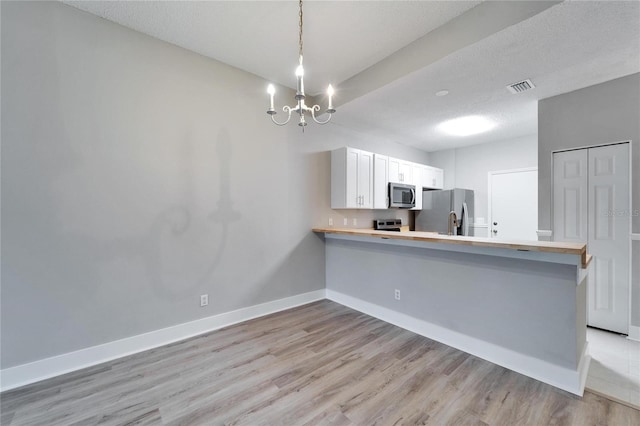 kitchen featuring kitchen peninsula, appliances with stainless steel finishes, decorative light fixtures, white cabinetry, and a textured ceiling