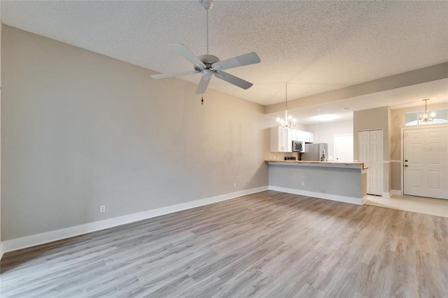 unfurnished living room featuring ceiling fan with notable chandelier, light hardwood / wood-style flooring, and a textured ceiling