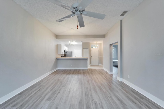 unfurnished living room featuring ceiling fan with notable chandelier, light hardwood / wood-style flooring, and a textured ceiling