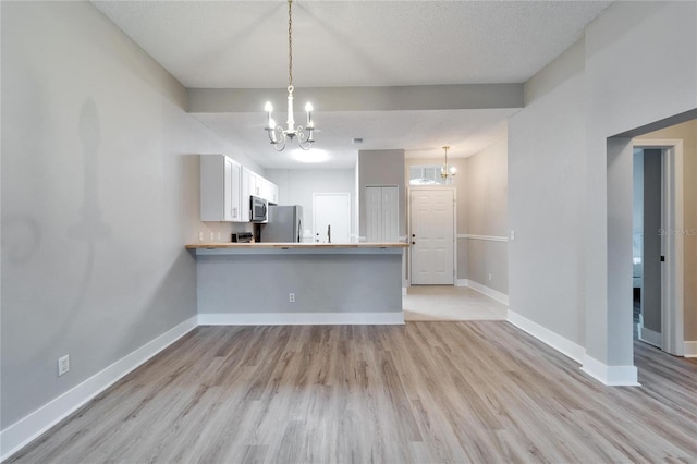 kitchen featuring kitchen peninsula, white cabinets, hanging light fixtures, and stainless steel appliances