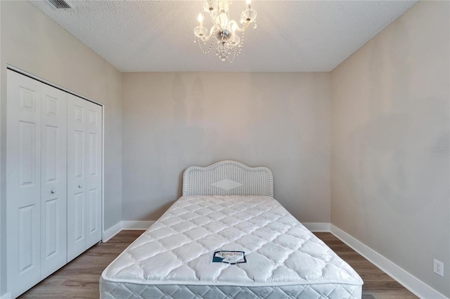 bedroom with hardwood / wood-style floors, a chandelier, a textured ceiling, and a closet