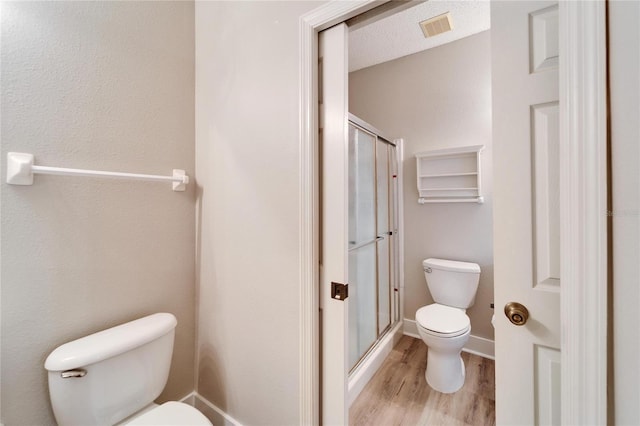 bathroom with wood-type flooring, toilet, a textured ceiling, and a shower with shower door