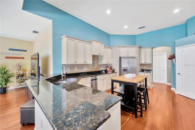 kitchen with appliances with stainless steel finishes, light hardwood / wood-style floors, sink, dark stone counters, and tasteful backsplash